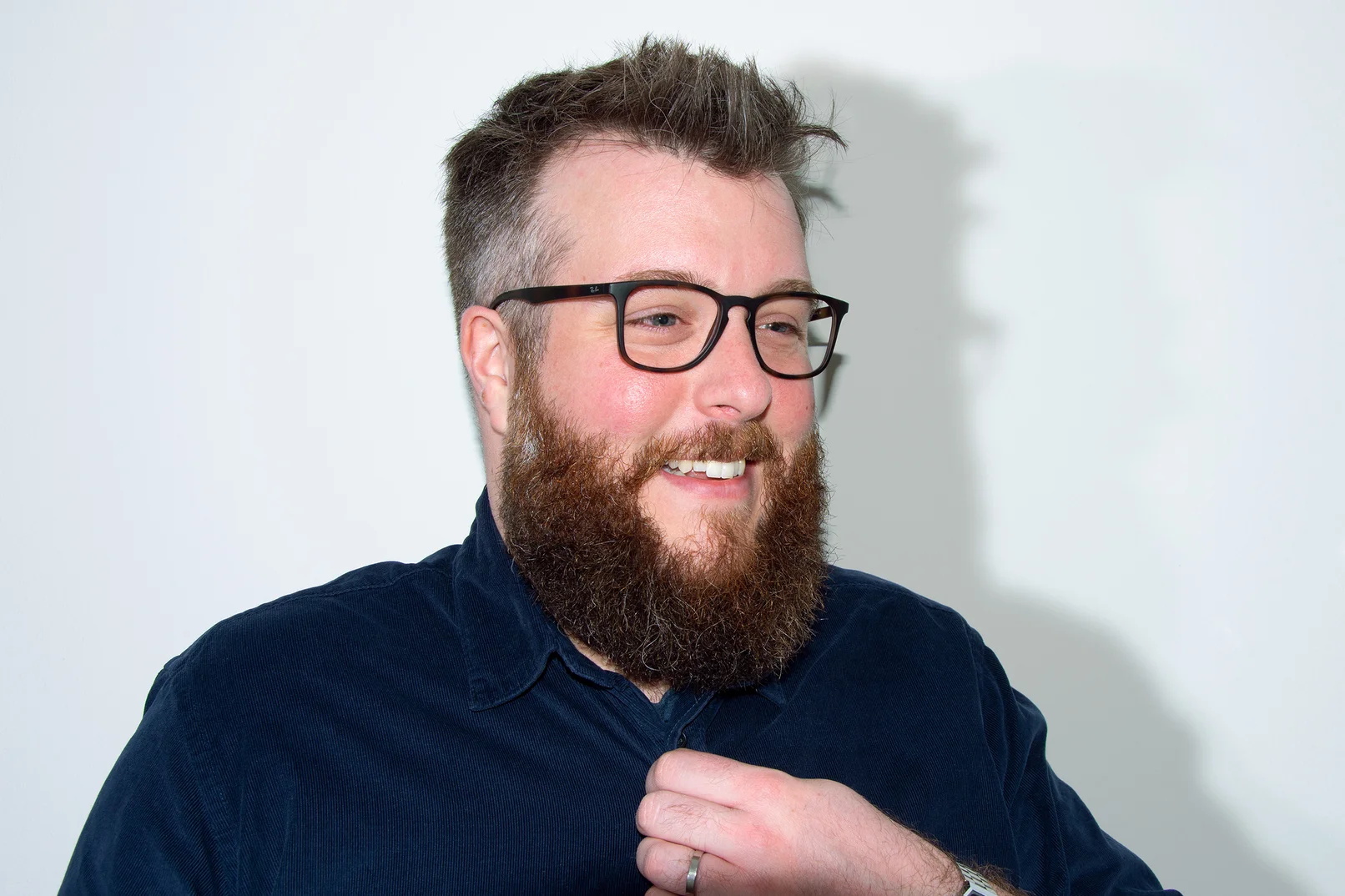 Mann vor weißem Hintergrund, der lachend an der Kamera vorbei schaut