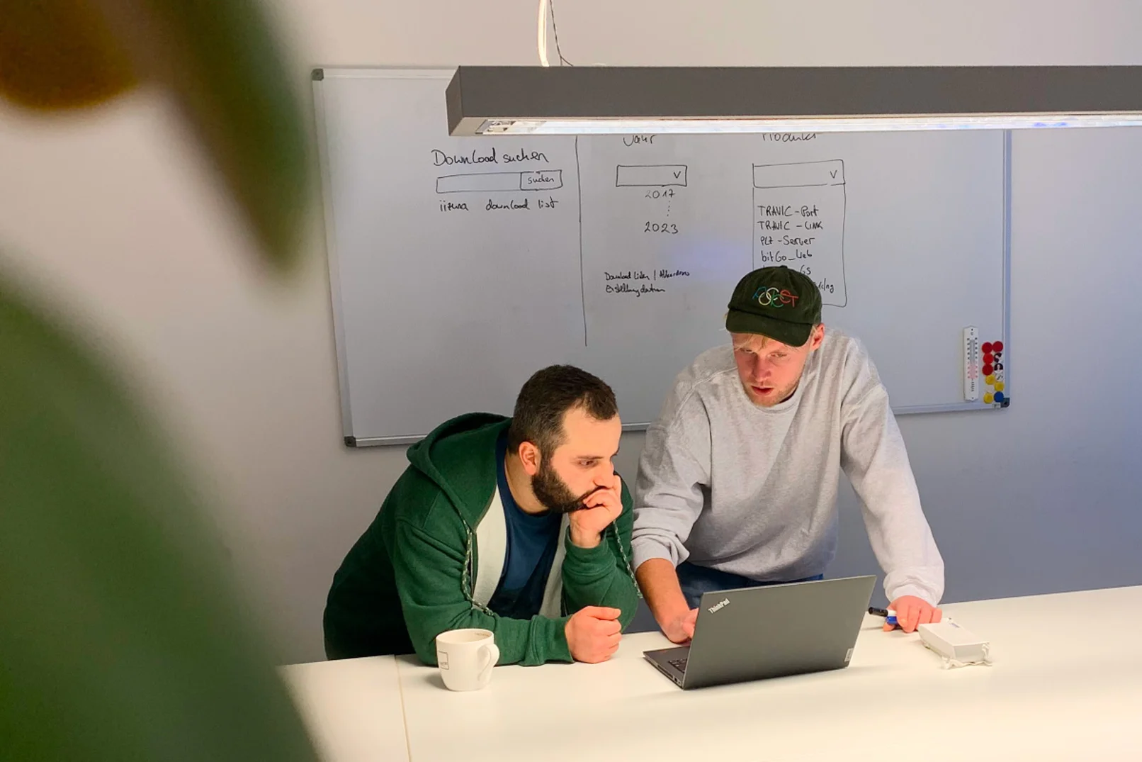 Zwei Entwickler schauen auf Laptop vor großem Whiteboard