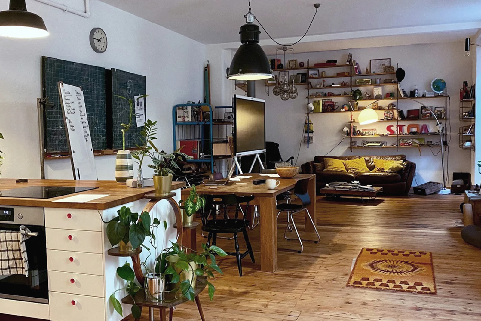 Raum mit Küchenzeile, Esstisch und Sofa mit vielen Pflanzen