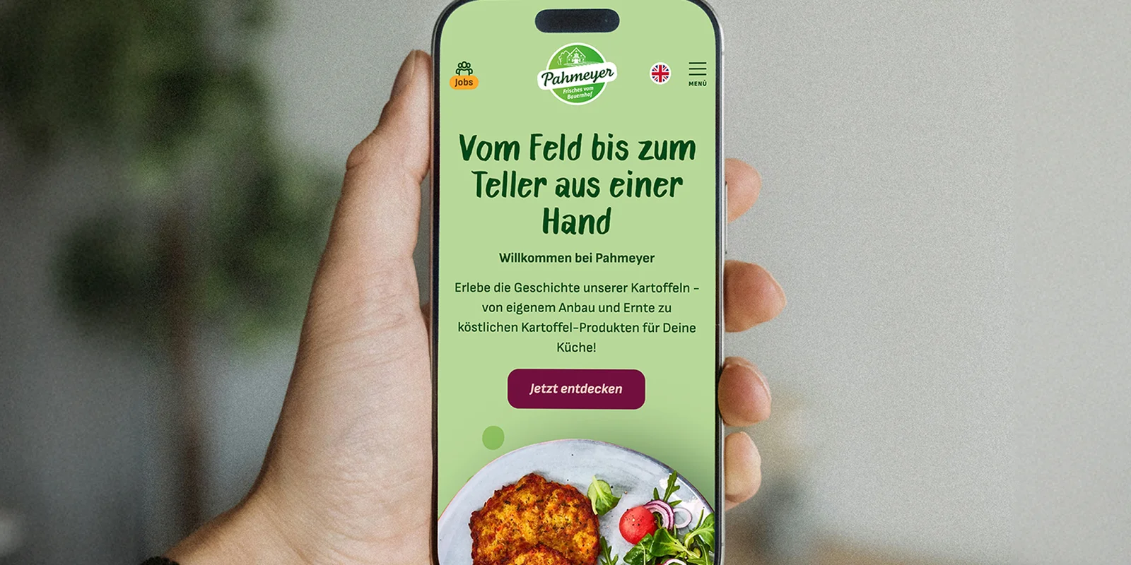 Hand hält Smartphone mit geöffneter Startseite der Pahmeyer-Website 